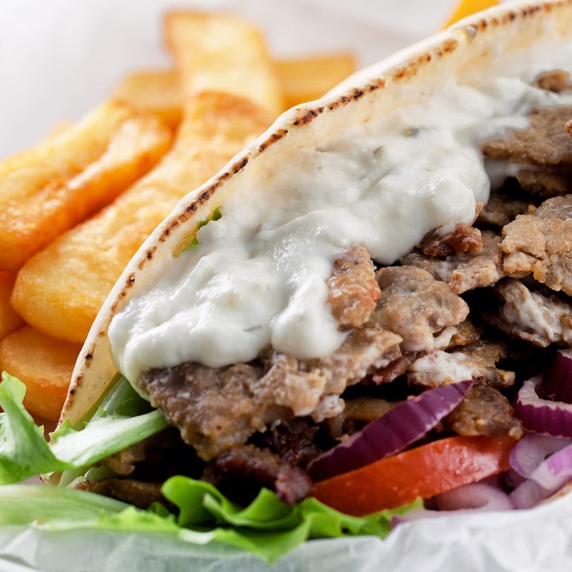 Gyro with meat, lettuce, tomato, red onion, and white sauce, served with fries.