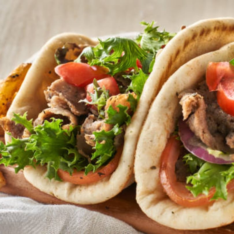 Two gyros with meat, lettuce, tomatoes, and onions in pita bread, served with fries.