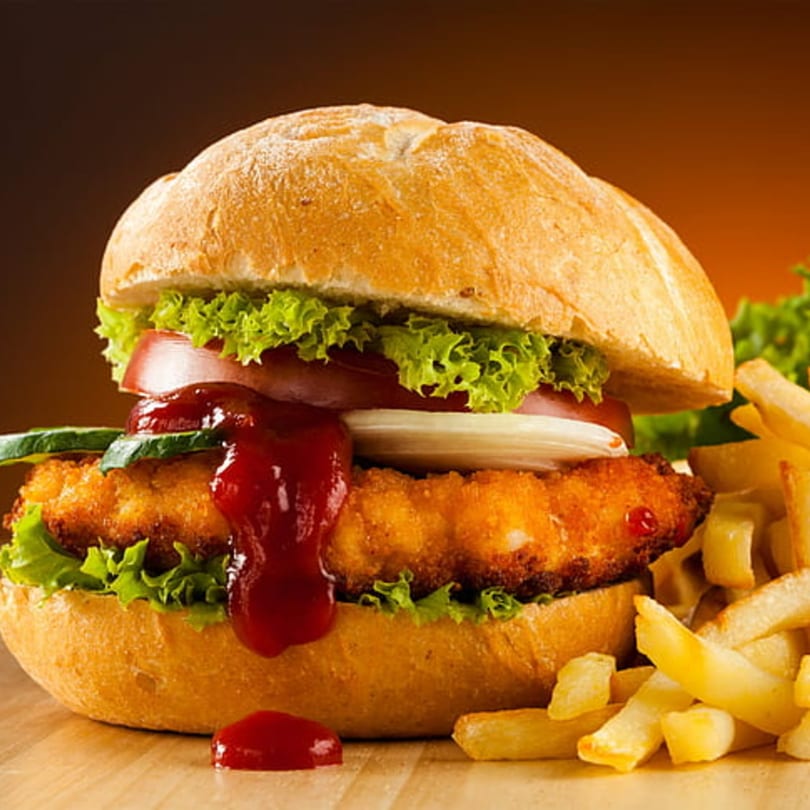 Crispy chicken sandwich with lettuce, tomato, onion, pickles, ketchup, and a side of fries.