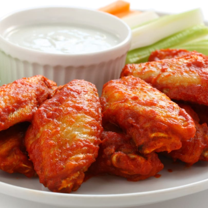 Spicy red buffalo wings with a side of blue cheese dip, celery, and carrot sticks.