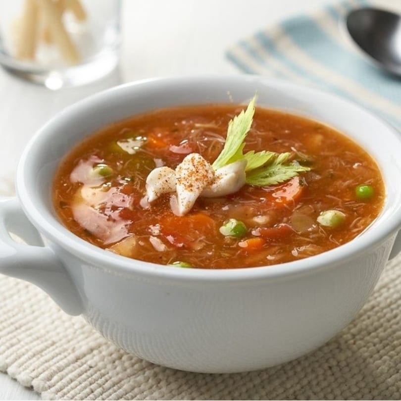 A white bowl of hearty vegetable soup with noodles, garnished with celery and spices.