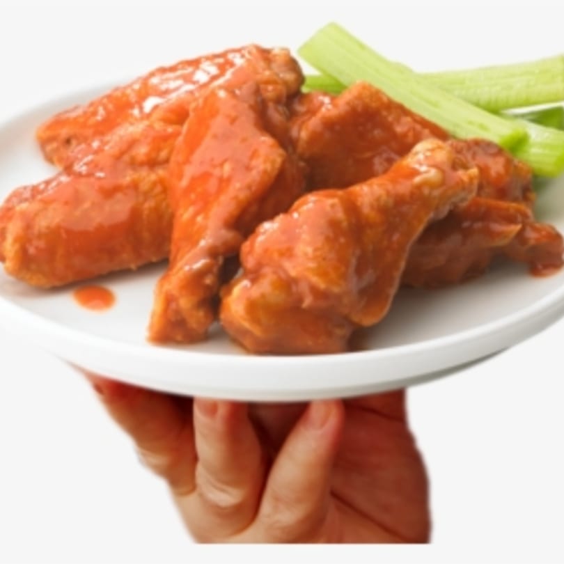 A hand holds a white plate of saucy buffalo wings with celery sticks on a white background.