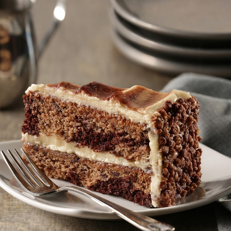 A slice of chocolate cake with white frosting and chocolate crumbles on a white plate with a fork.