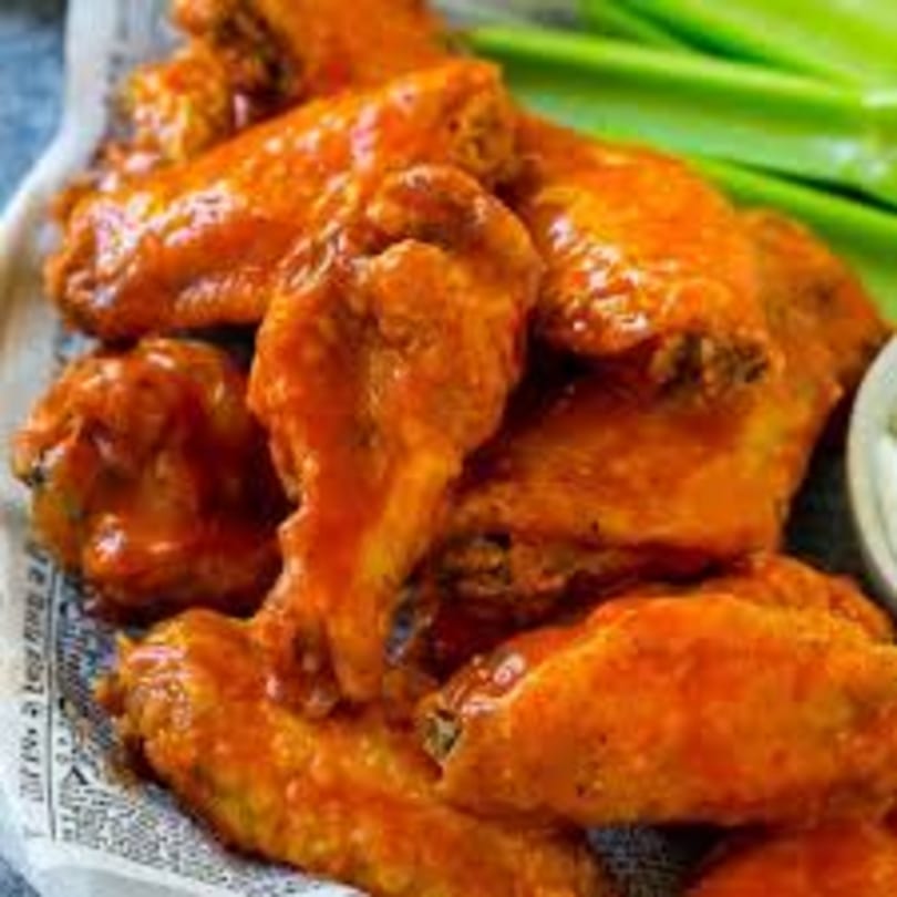 A close-up of saucy buffalo chicken wings with celery sticks and ranch dressing.