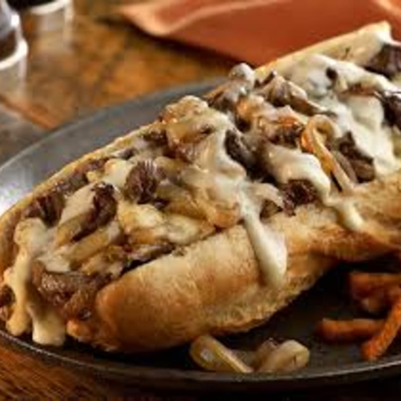 A Philly cheesesteak sub with melted cheese, steak, and onions on a dark plate.