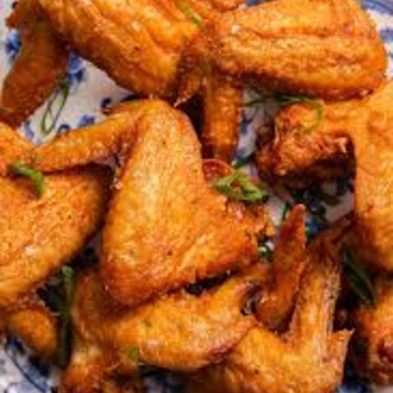 Crispy golden-brown chicken wings, garnished with green onions, piled on a white and blue patterned plate.