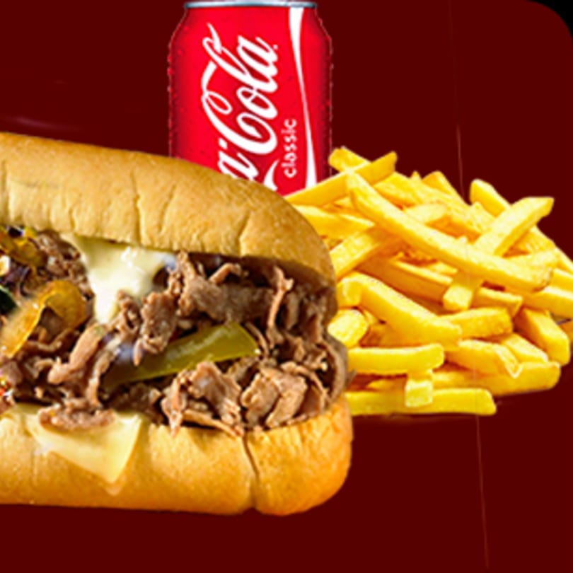 Philly cheesesteak sub with melted cheese, onions, and peppers, alongside fries and a Coca-Cola can.