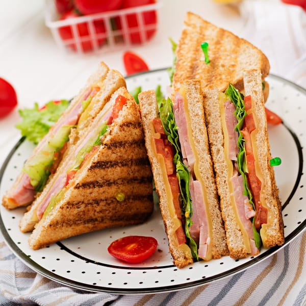 Two toasted club sandwiches with ham, cheese, lettuce, and tomato on a polka-dotted plate.