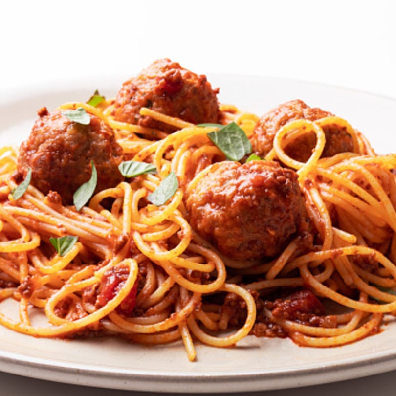 Spaghetti and meatballs with tomato sauce and fresh basil on a white plate.