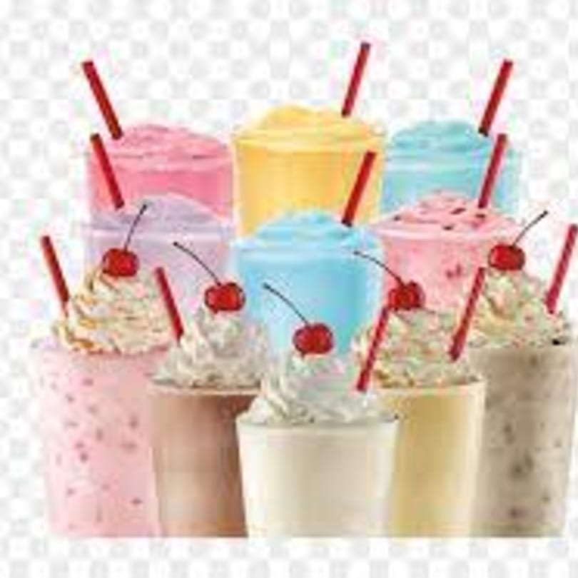 Assortment of colorful milkshakes with whipped cream, cherries, and red straws.