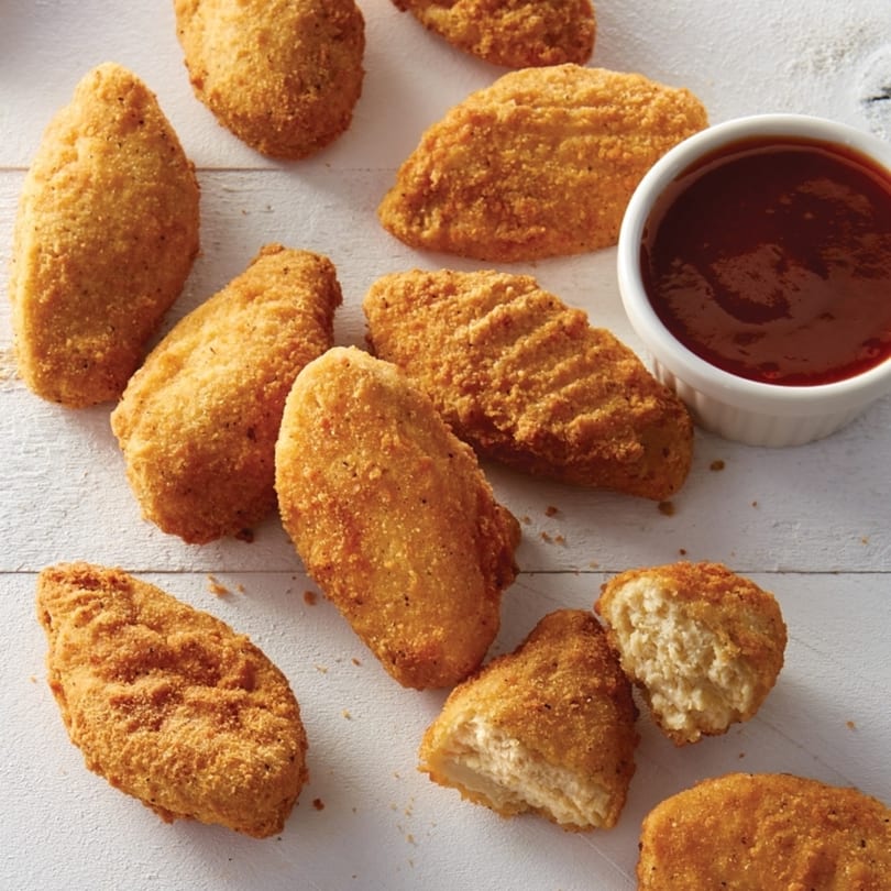 Crispy golden chicken nuggets, some with bites taken, and a side of barbecue dipping sauce.