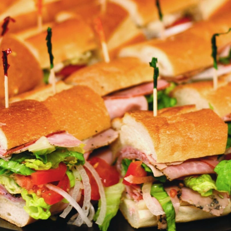 Platter of Philly's Best Subs, cut in half, filled with meat, cheese, lettuce, tomatoes, and onions.